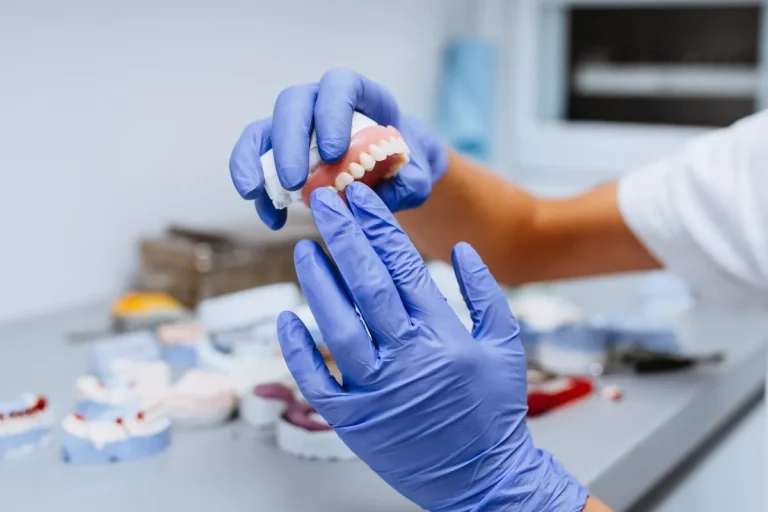 Dental prosthesis, prosthetics work. Close up of prosthetic's hands while working on the denture. Selective focus.