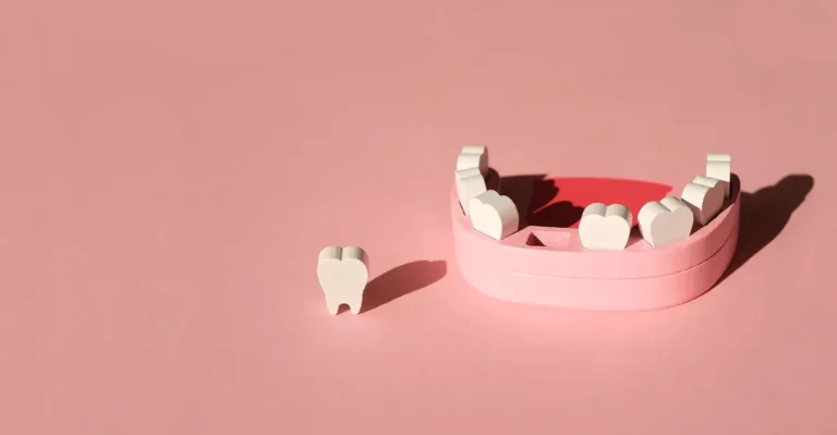 Wooden model of a human jaw with a missing tooth on a pink studio background. The problem of tooth loss. Baby milk teeth. Banner.